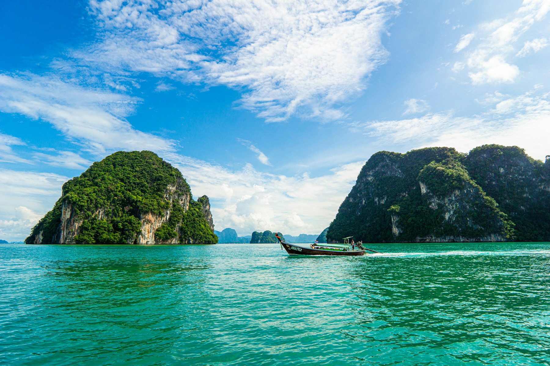 A longtail boat crossing turquoise water between Thailand's limestone islands